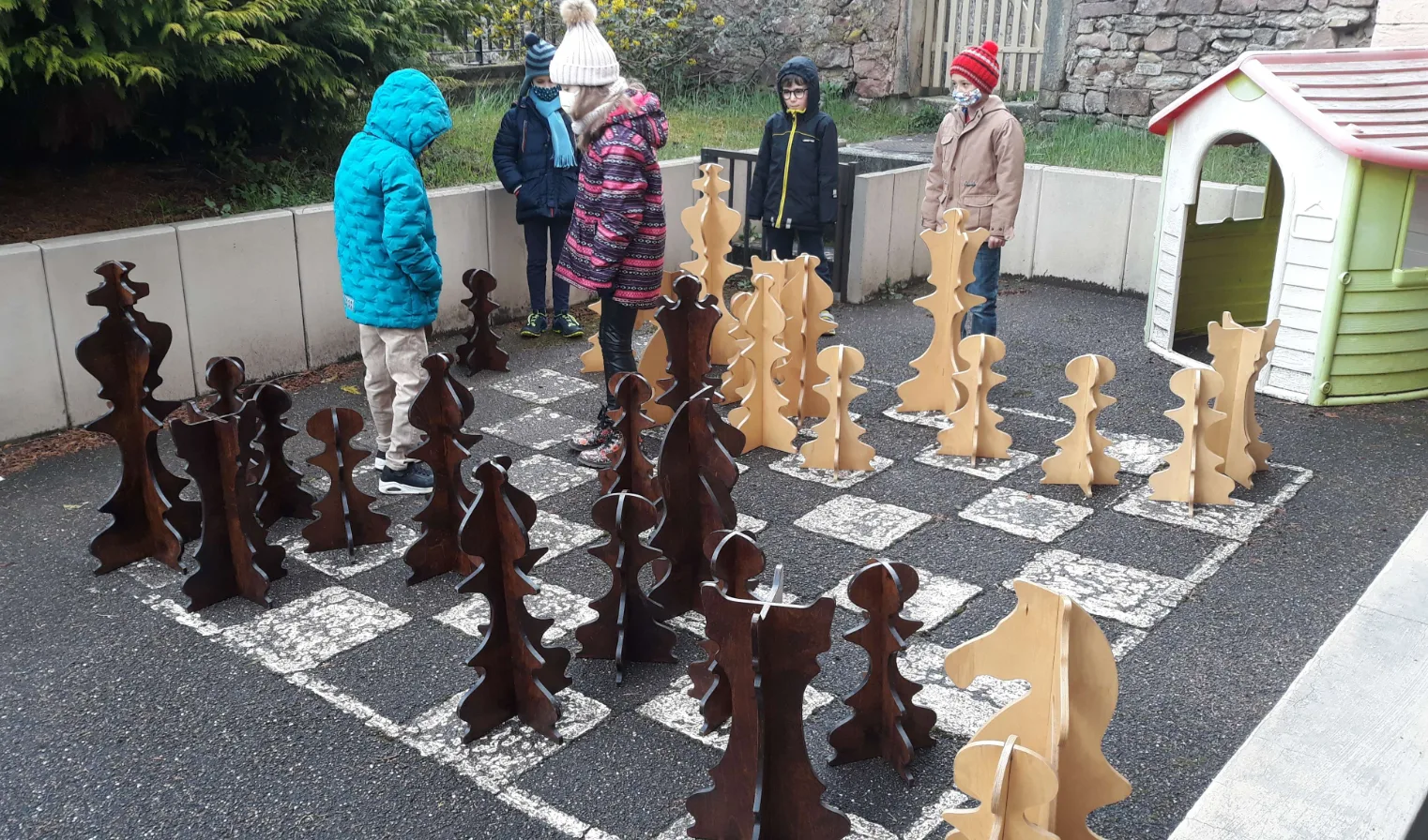 Des enfants déplacent des pièces géantes sur l'échiquier peint dans la cour de l'école